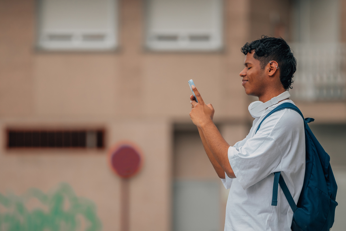 young latino man with mobile phone and backpack in the street